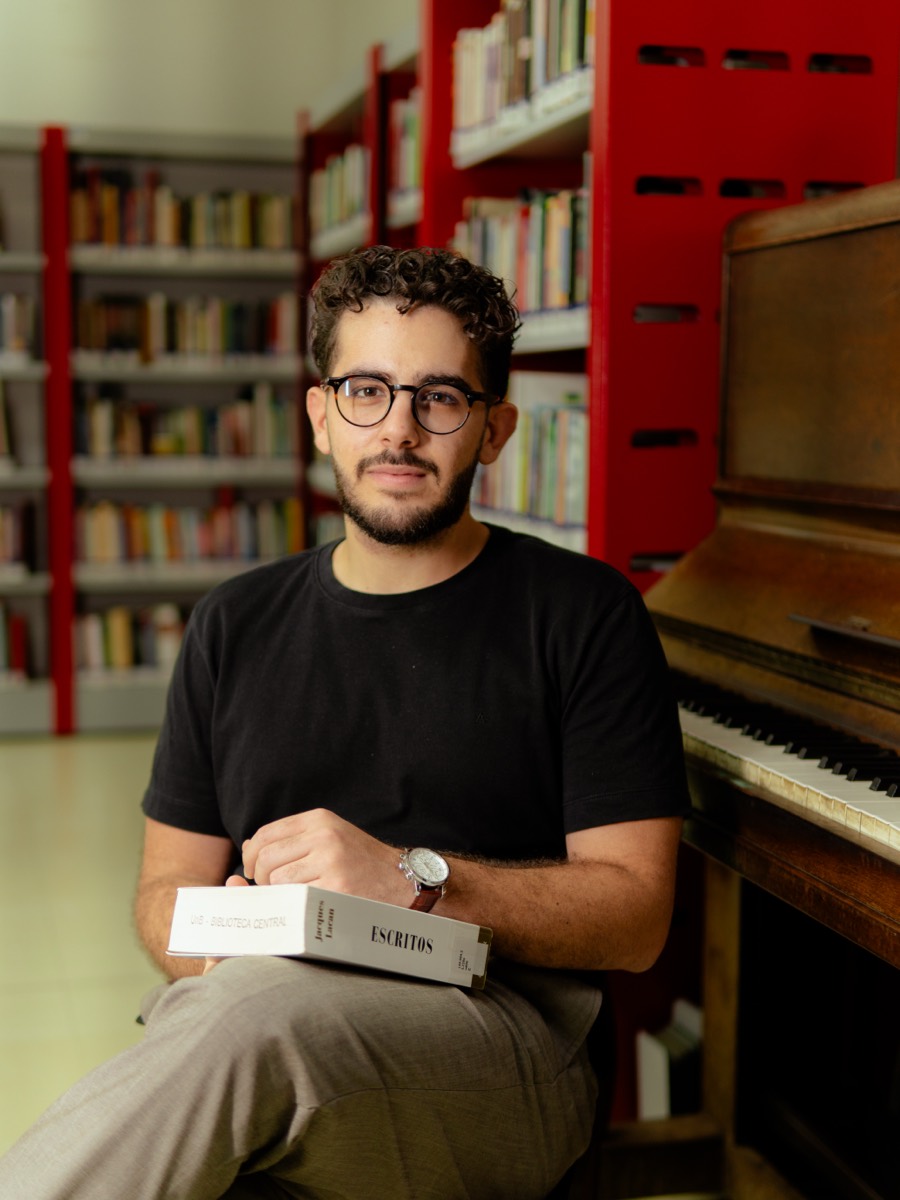 Arthur Pires na Biblioteca Central da UnB, com os Escritos de Lacan, ao lado de um piano